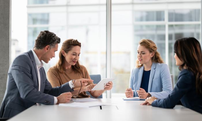 Ein Mann und drei Frauen in Business Kleidung sitzen in einem Besprechungsraum und reden miteinander