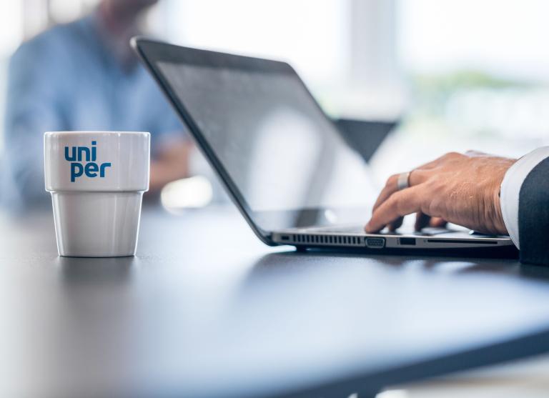 Employee working at laptop with Uniper branded cup next to him