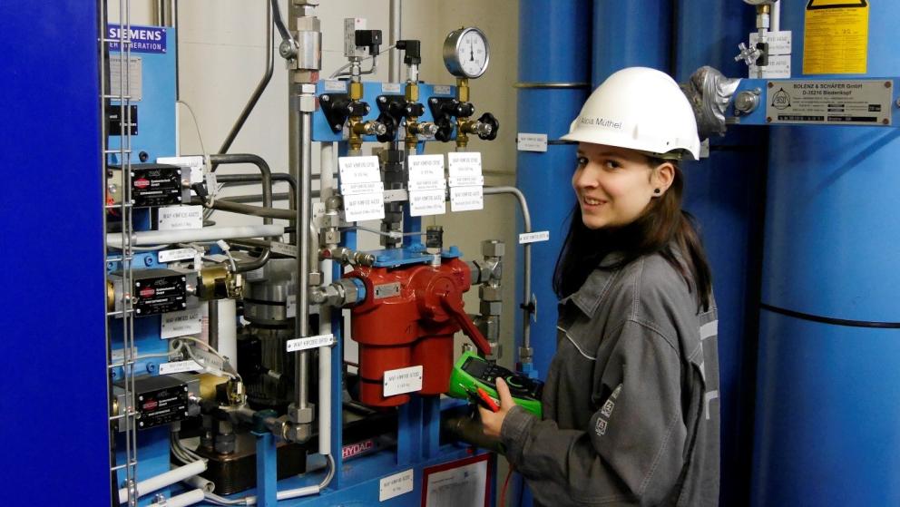 Weibliche Auszubildende mit Helm steht im Kraftwerk an Maschine